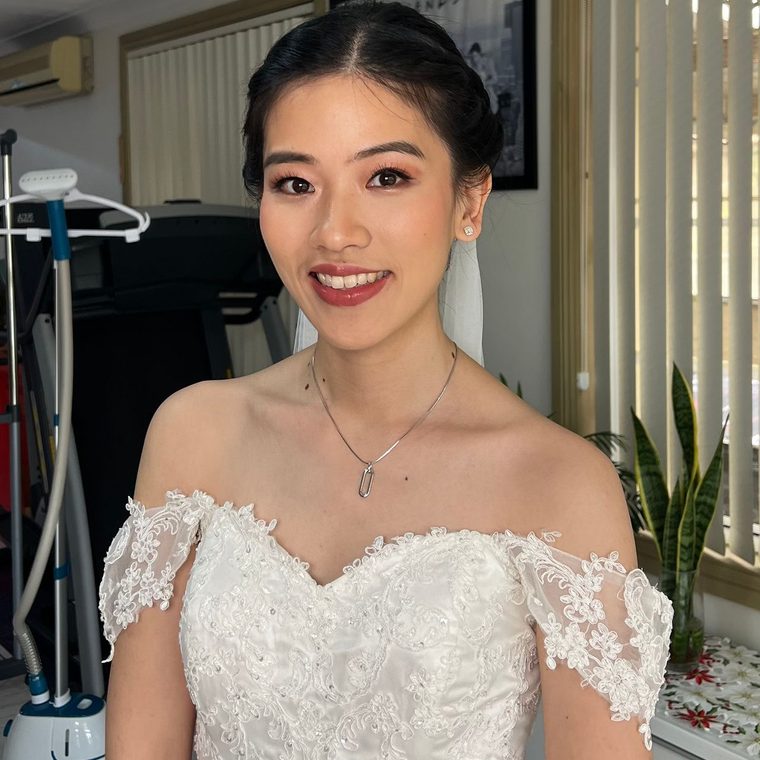 A bride in an off-shoulder lace gown, soft glam and a low bun